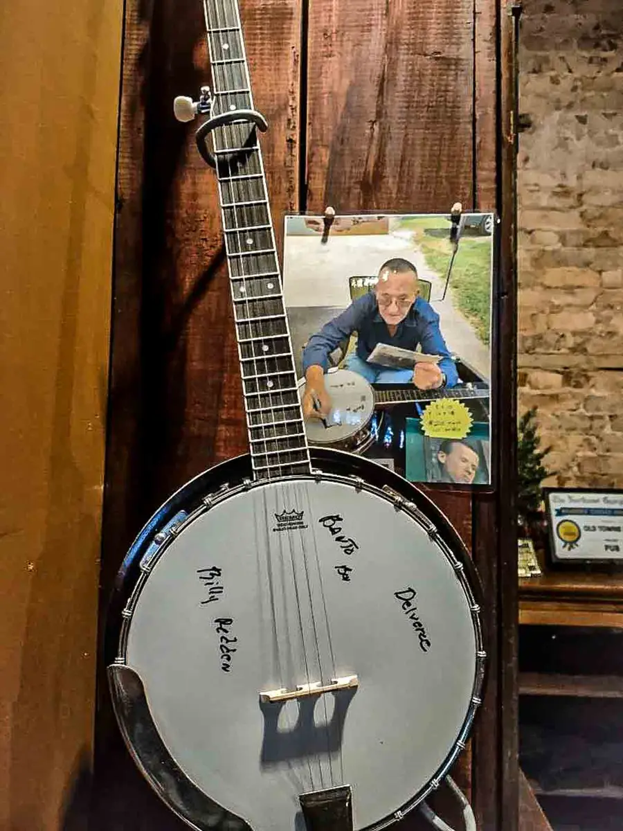 A banjo hanging on the brick wall at Old Towne Pub, signed by Billy Redden, beside a framed photograph of him
