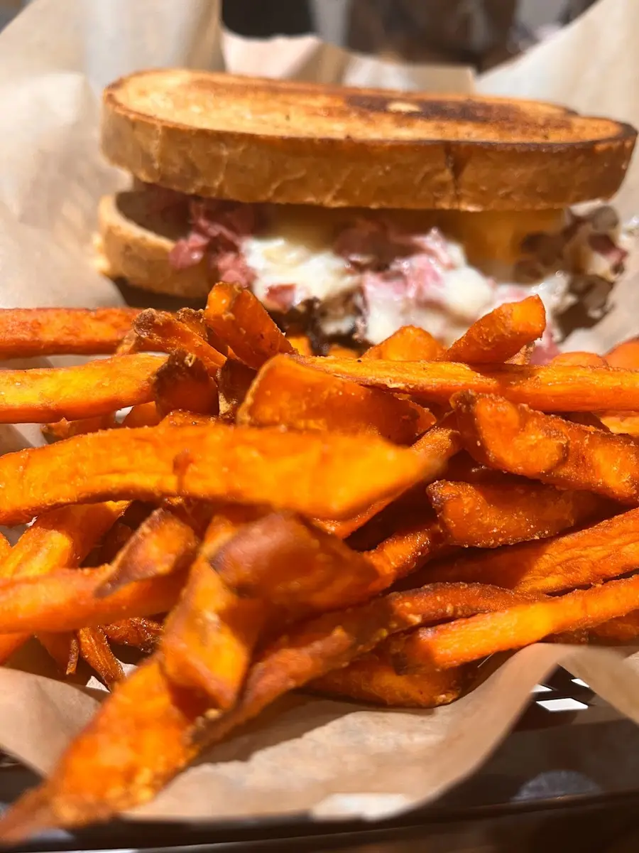 A reuben on marbled rye served with a basket of sweet potato fries