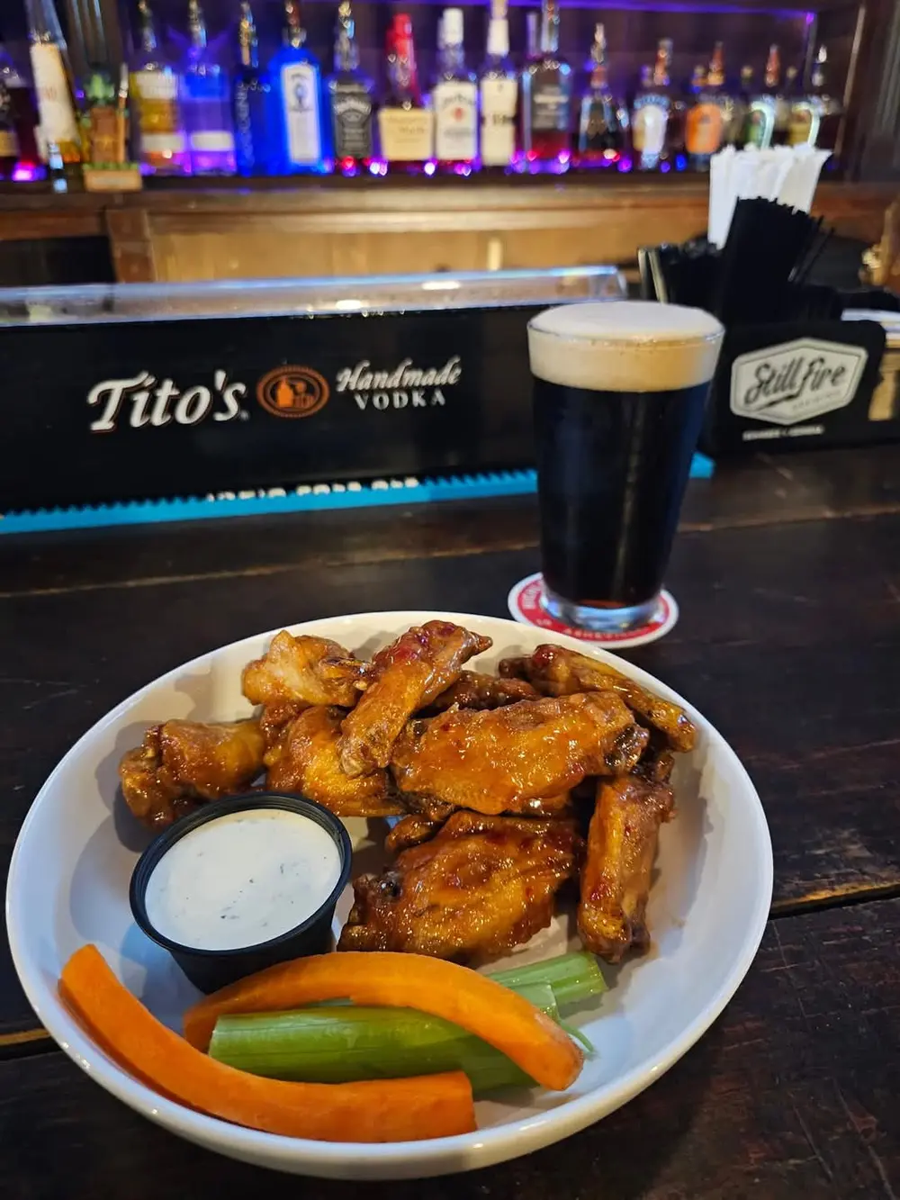 A plate of sauced wings with celery sticks next to a cold beer on the bar